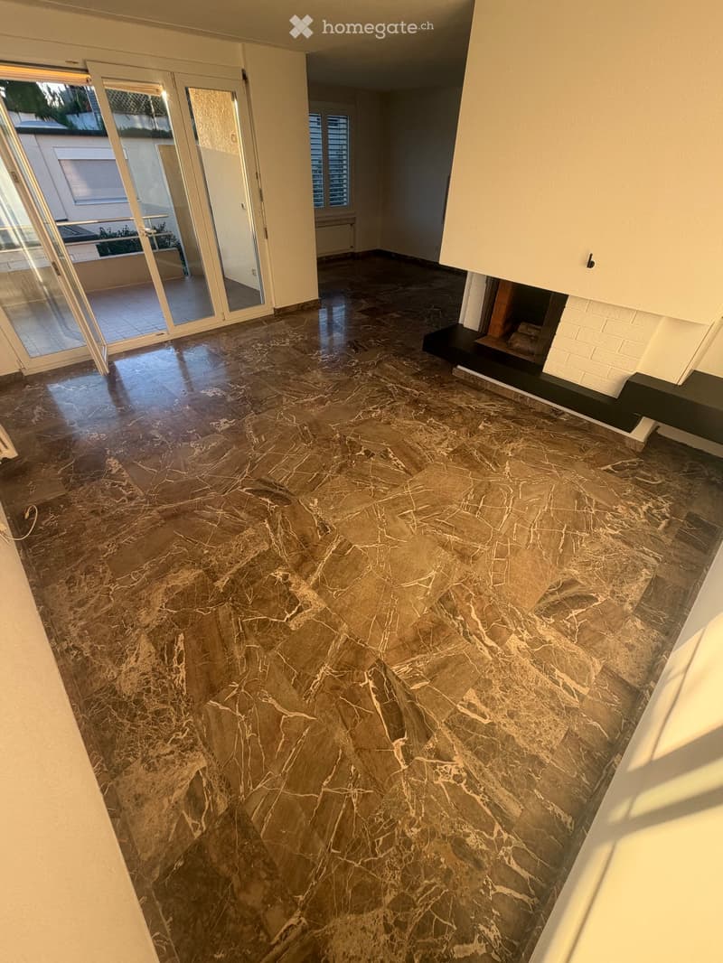 Empty room with polished marble flooring, white walls, and a fireplace with a black platform. Large glass sliding doors lead to a balcony or outdoor area.