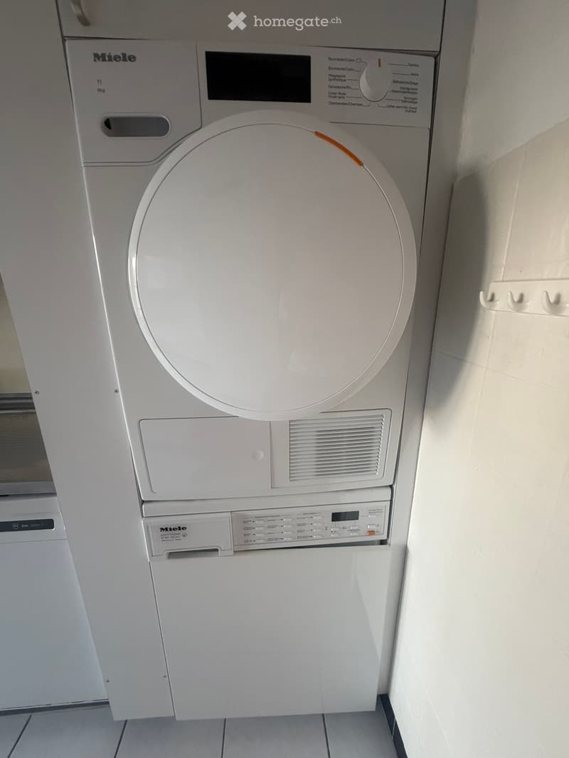 White Miele washing machine and dishwasher stacked vertically in a bathroom corner.