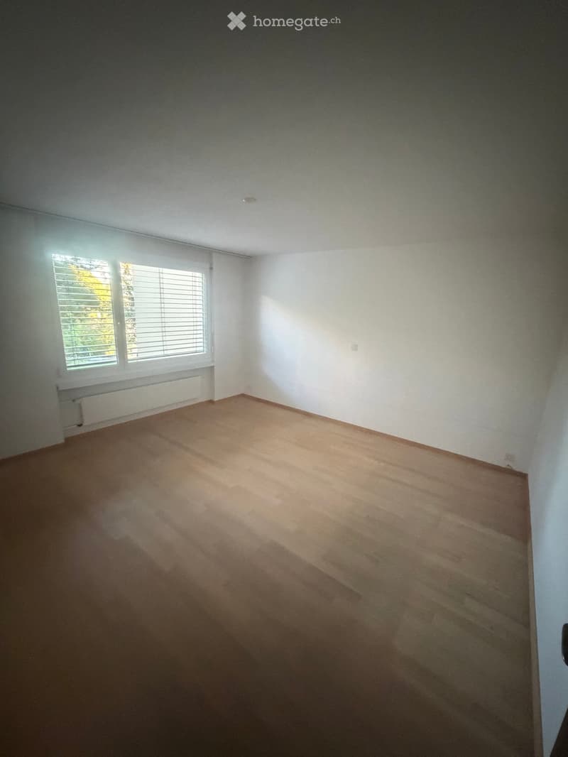 Empty room with wooden flooring, white walls, and a large window with blinds. No furniture or equipment is present.