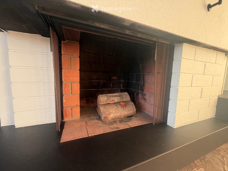 Fireplace with brick surround, log inside, and a metal screen in front.