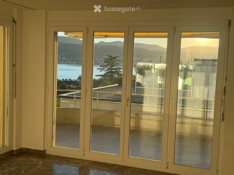 Large sliding glass doors open to a balcony with a scenic view of a lake and distant mountains.