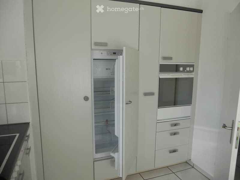 Modern kitchen with white cabinets, an open refrigerator, and an oven. The refrigerator door is open, revealing its interior shelves and drawers.
