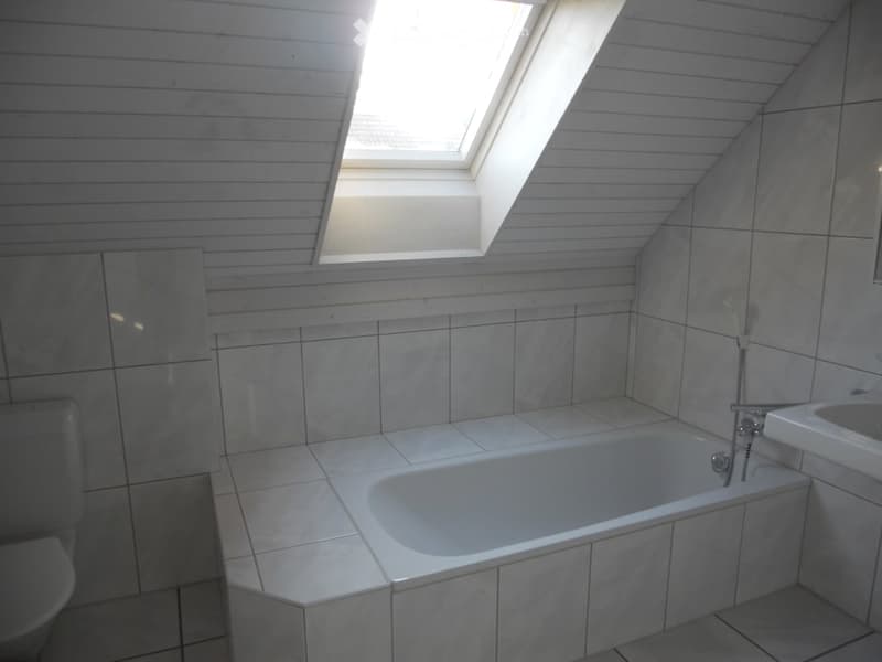 Bright bathroom with a skylight window, tiled walls and floor, bathtub, toilet, and sink.