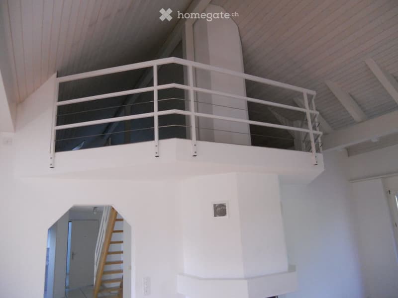 Open loft-style balcony with white railings and wooden ceiling beams, overlooking a central living space.
