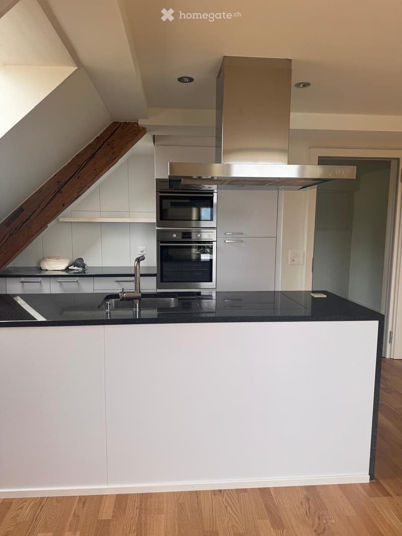 Modern kitchen with white cabinets, stainless steel appliances, black countertop, and wooden flooring.