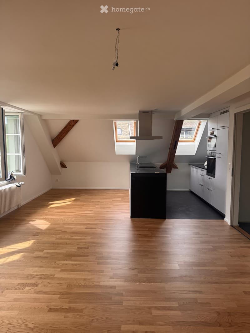 Bright, airy kitchen with wooden flooring, white cabinets, a black island, and a stainless steel range hood. Natural light streams in from multiple windows, including a skylight.