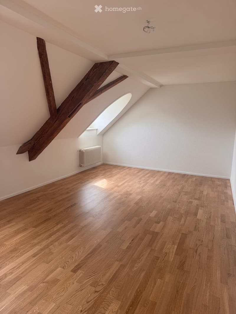 Empty attic room with wooden floors, exposed wooden beams, and skylight windows providing natural light.