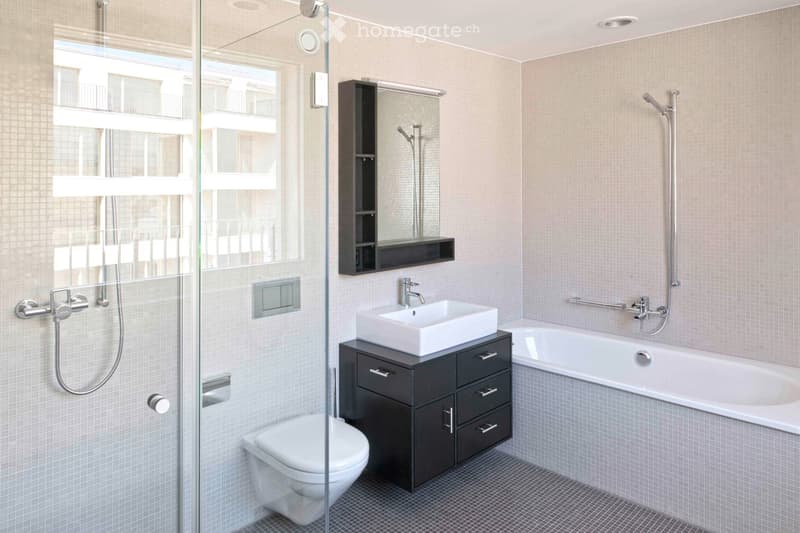 Modern bathroom with a white sink, dark wooden cabinet, bathtub, toilet, and a large mirror with built-in storage. The shower area has a glass enclosure and a handheld showerhead.