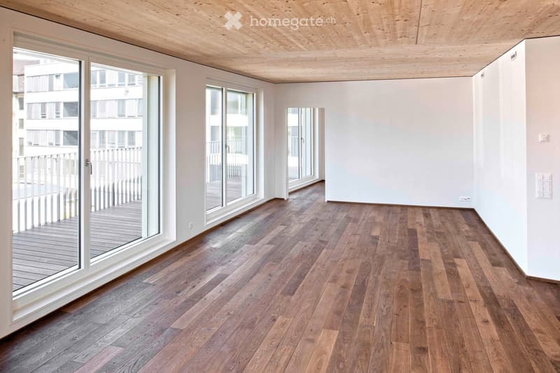Empty room with wooden flooring, white walls, large glass sliding doors leading to a balcony, and a wooden ceiling.