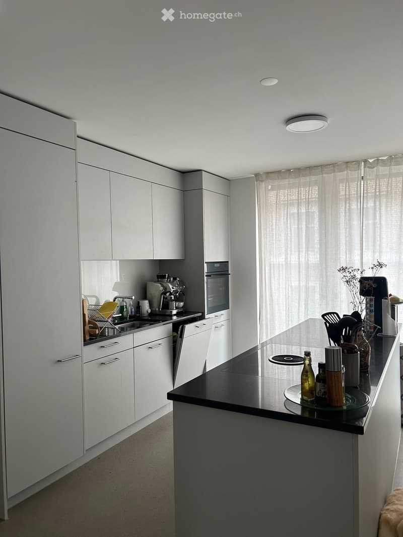 Modern kitchen with white cabinets, black countertop, stainless steel appliances, and various kitchen items on the counter.