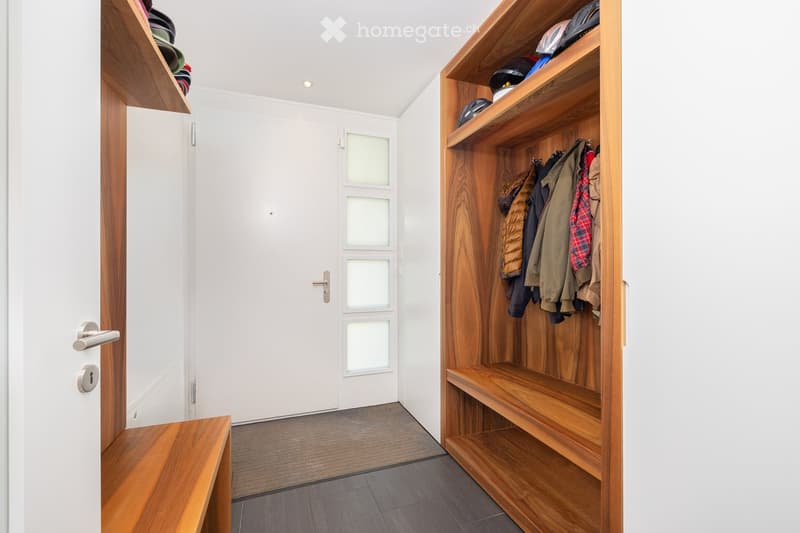 Modern hallway with built-in wooden shelving unit, coats hanging, and a white door with frosted glass panels.