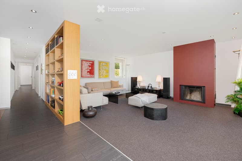 Modern living room with a fireplace, grey sofa, ottoman, coffee table, bookshelf, table lamps, speakers, and decorative items.