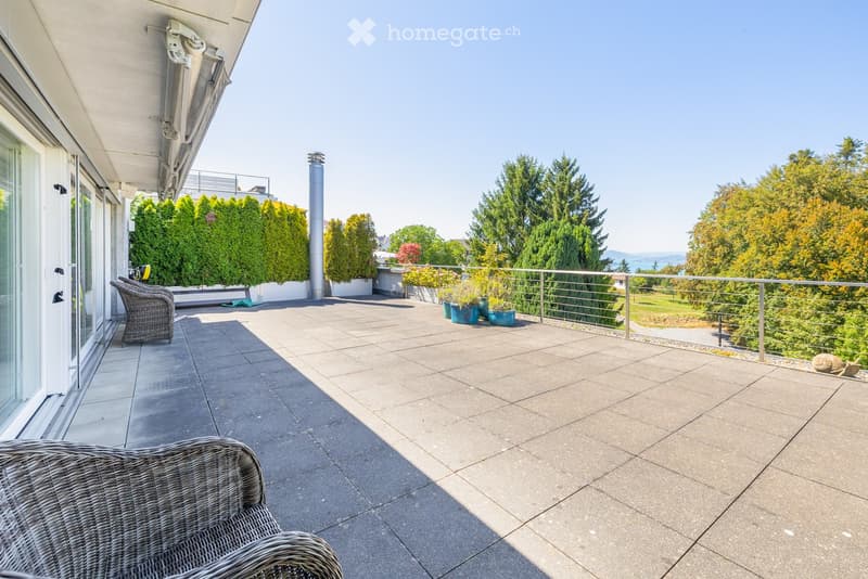 Balcony with tiled floor, metal railing, two wicker chairs, and potted plants.