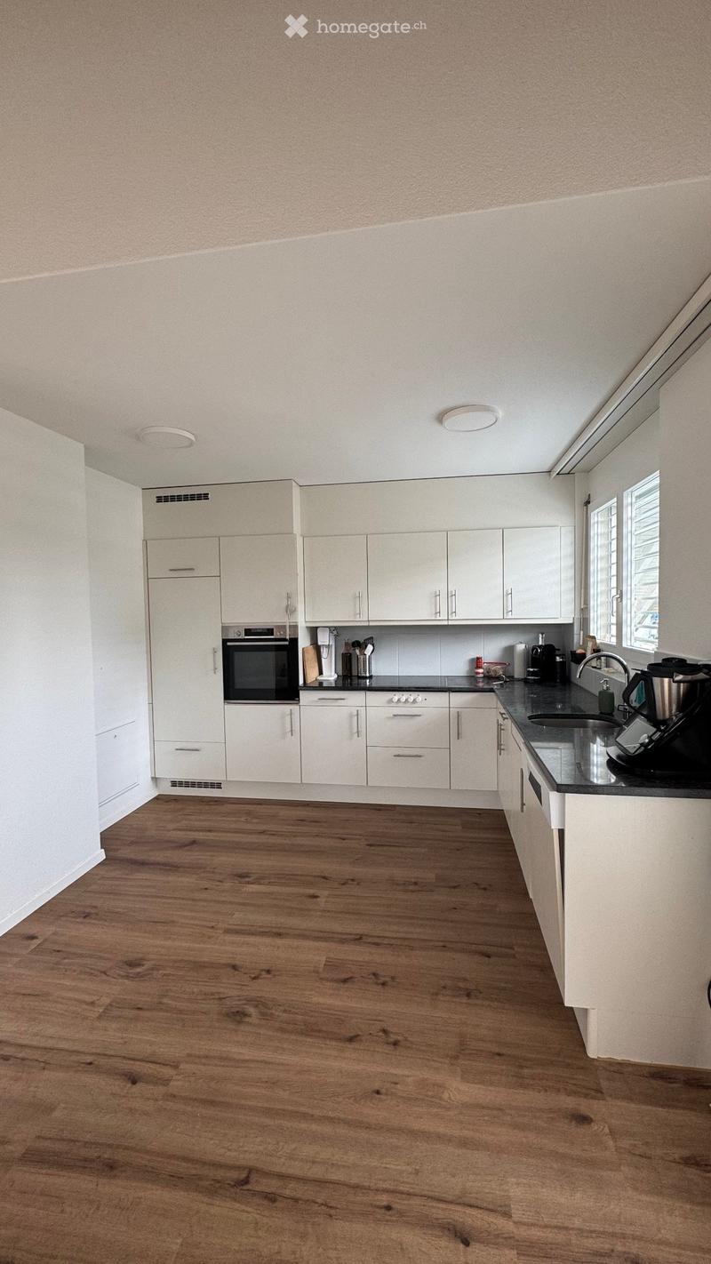 Modern kitchen with white cabinets, wooden flooring, and stainless steel appliances including an oven and coffee maker.