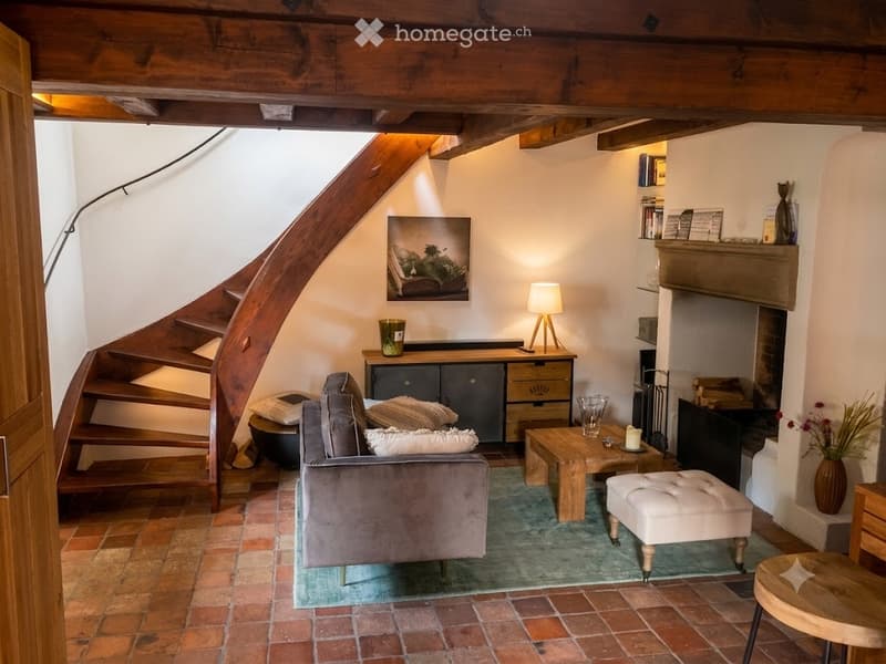 Cozy living room with exposed wooden beams, brick floor, fireplace, sofa, ottoman, coffee table, floor lamp, and cabinet.