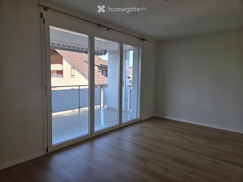Empty room with wooden flooring, large sliding glass doors leading to a balcony, and light-colored walls.