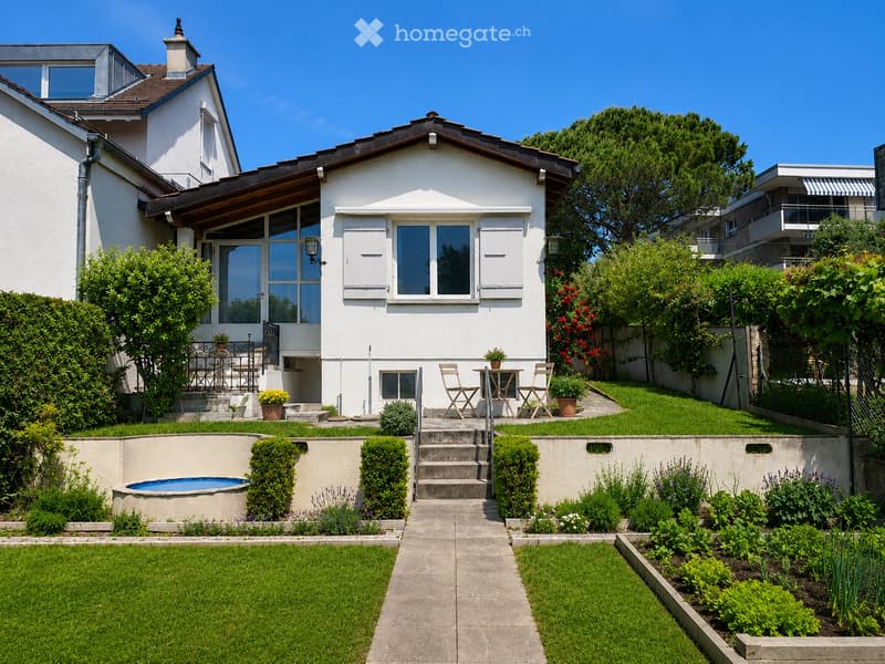 Well-maintained garden with a small swimming pool, neatly trimmed hedges, flower beds, and a patio area with outdoor furniture.