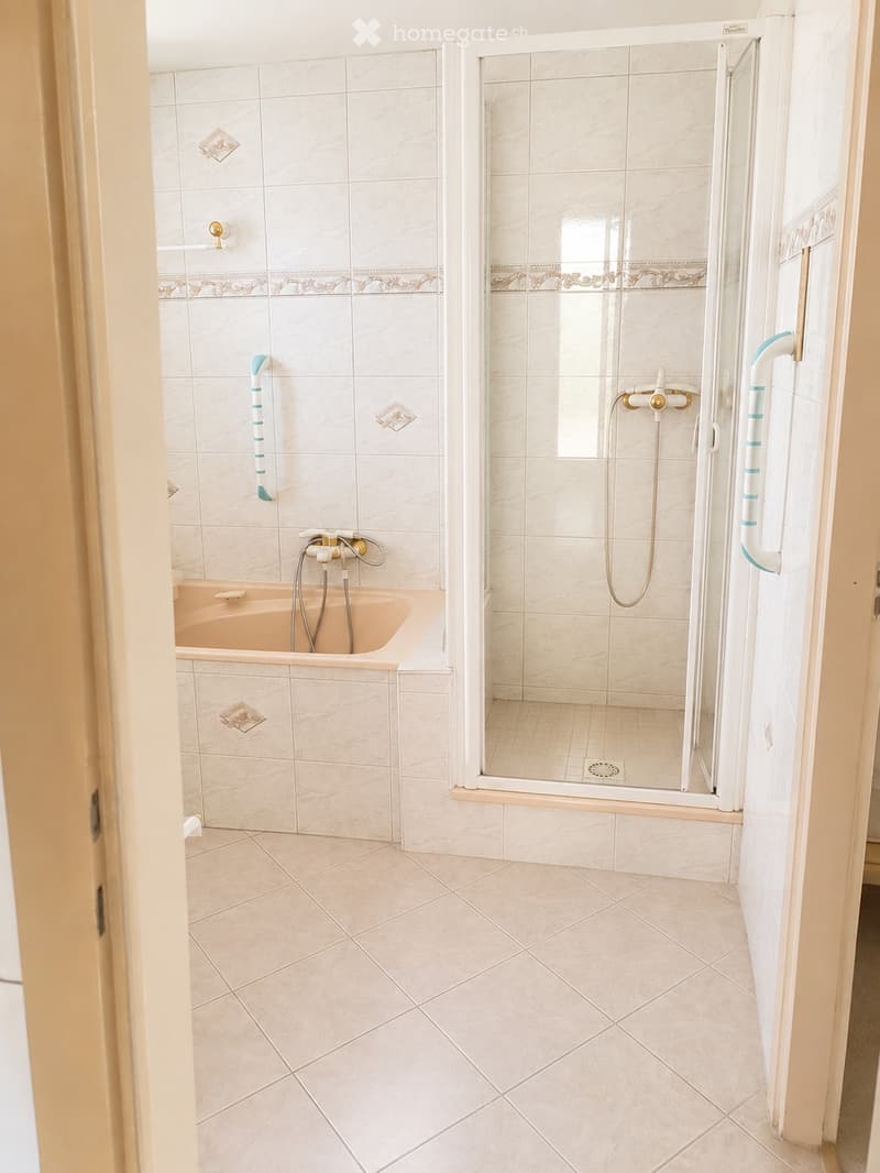 Modern bathroom with a bathtub and a separate shower area, featuring white marble tiles and a glass shower enclosure.