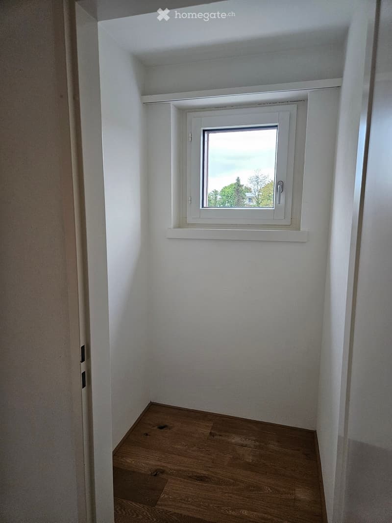 Empty room with white walls, wooden floor, and a single window with white frame and blinds.