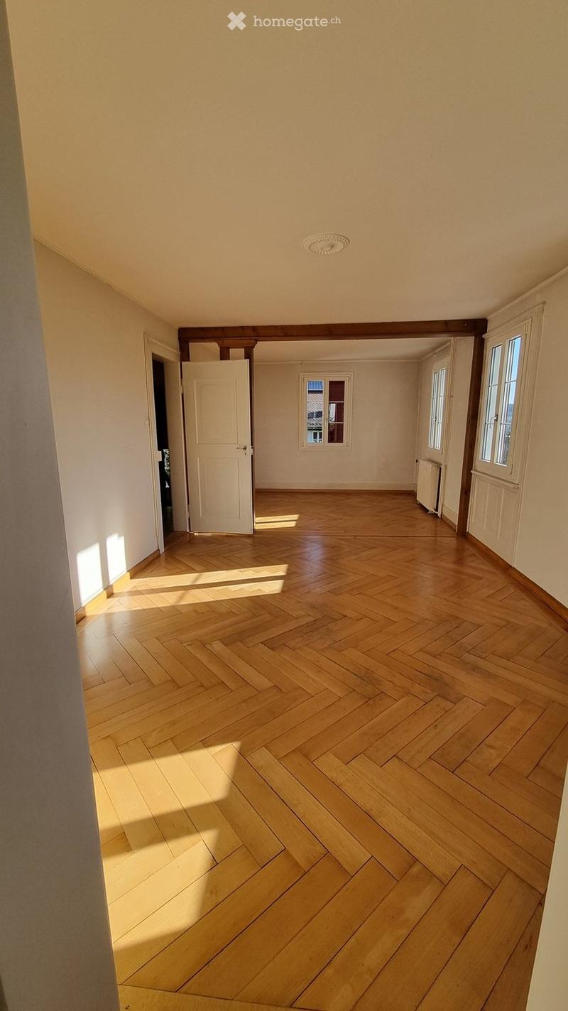 Empty room with wooden herringbone flooring, white walls, and natural light from windows. No furniture or equipment present.