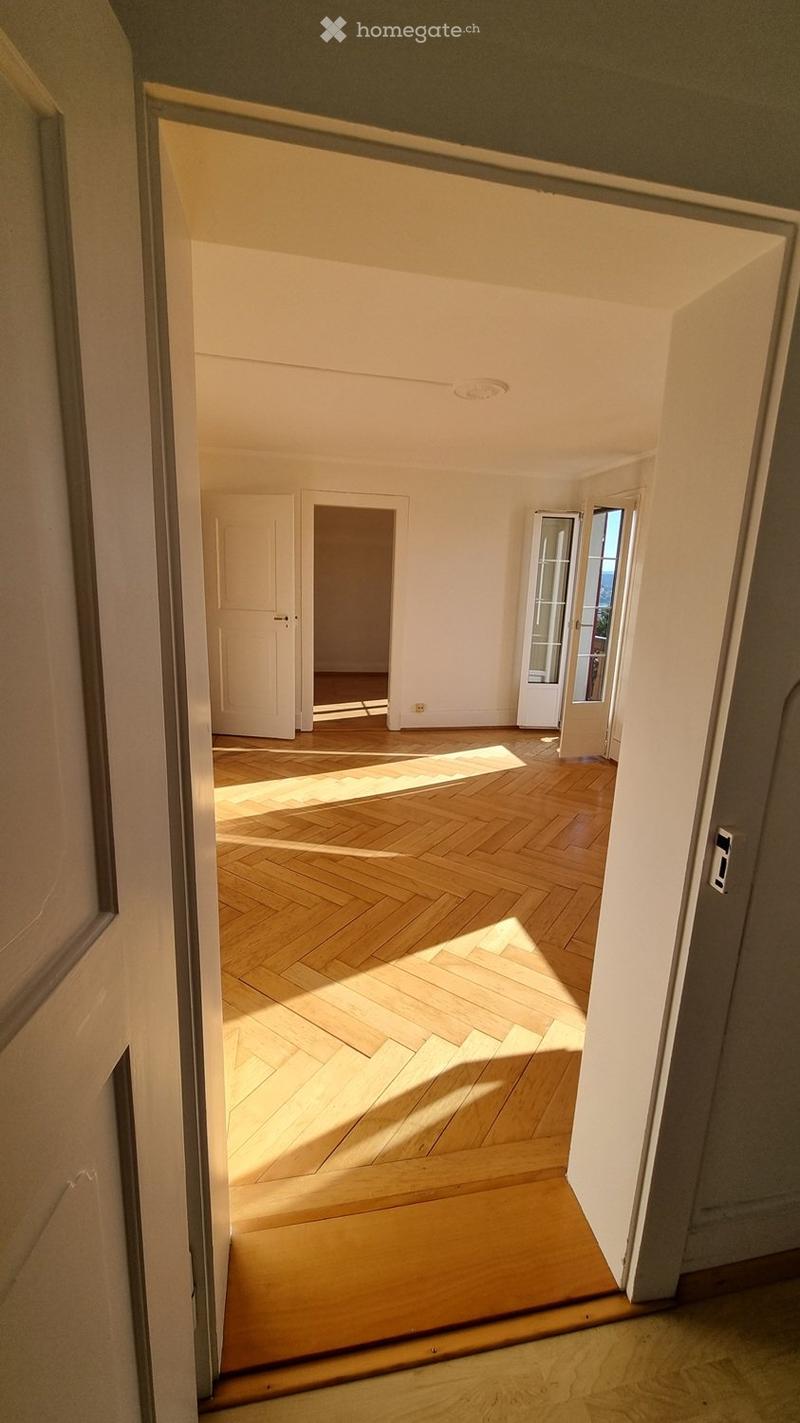Empty room with wooden flooring and white walls, featuring an open doorway leading to another room with similar flooring and white walls.