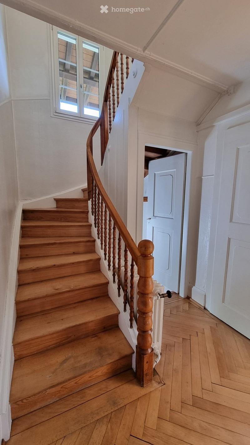 Wooden staircase with a wooden handrail and balusters, leading up to a landing with a window and a door.