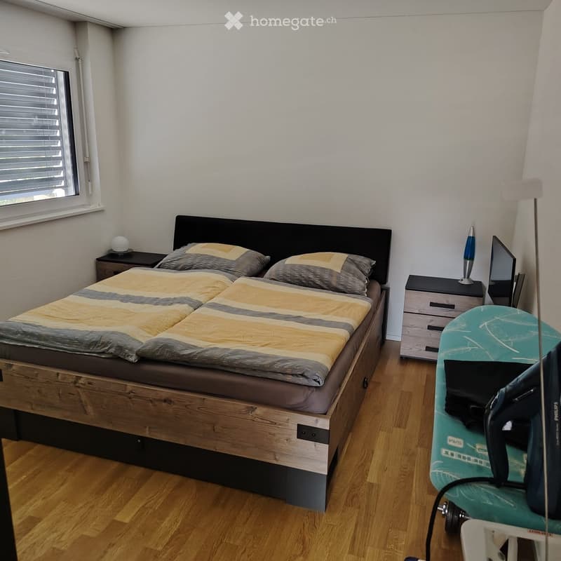 Cozy bedroom with a wooden bed, nightstands, a lamp, and a surfboard leaning against the wall.