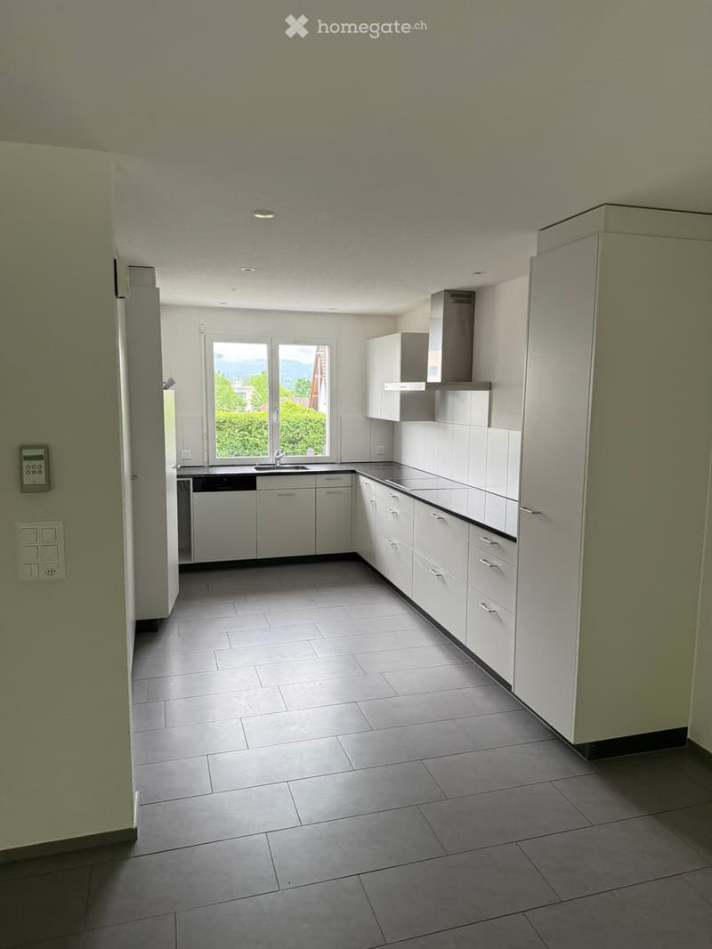 Empty kitchen with white cabinets, stainless steel appliances, tiled floor, and large windows offering a view of greenery.