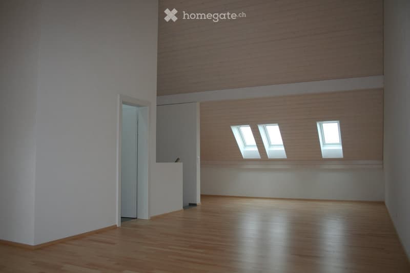 Large room with wooden floor, white walls, three windows, and wooden beams on the ceiling