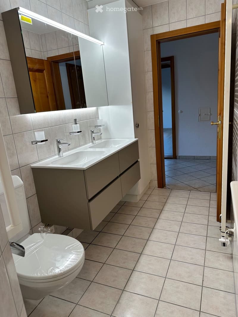 Modern bathroom with beige tiles, double sink vanity, mirror with LED lighting, and a toilet.