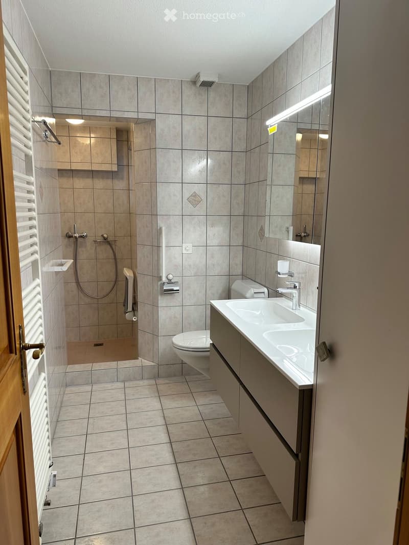 Modern bathroom with beige tiles, double sink, toilet, shower, and built-in cabinet.