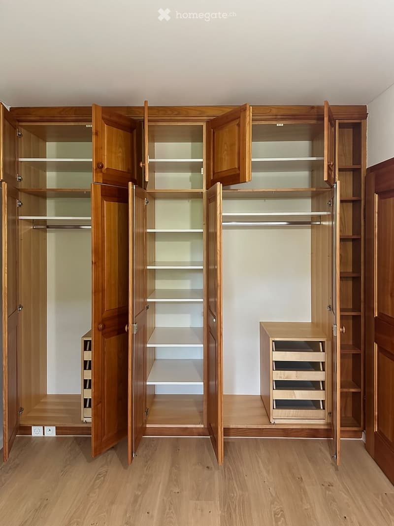 Empty room with wooden floor and large, open wooden wardrobes with shelves and drawers.