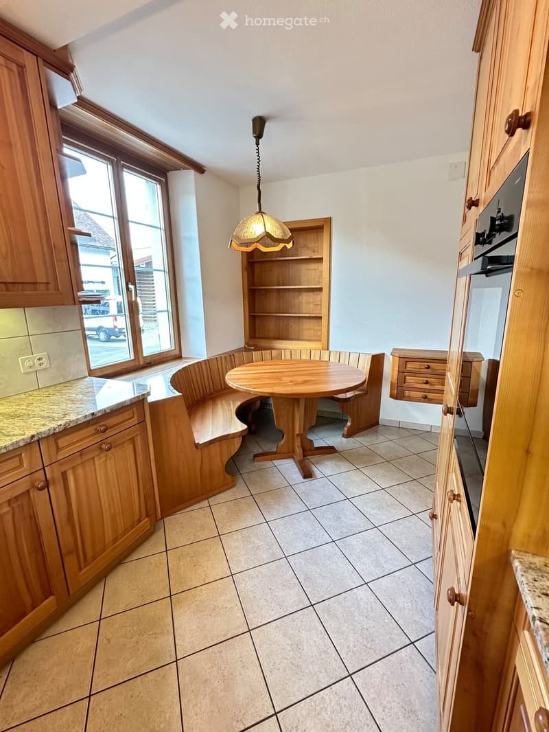 Bright kitchen with wooden cabinets, granite countertops, a round wooden table with a built-in bench seating, and a pendant light fixture.
