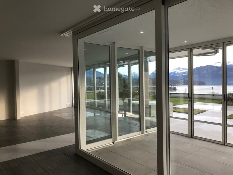 Modern hallway with large glass sliding doors leading to a scenic outdoor area, featuring a tiled floor and white walls.