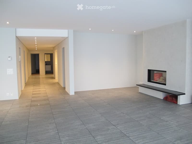 Empty hallway with tiled floor, white walls, recessed lighting, and a built-in fireplace with a bench on one side.