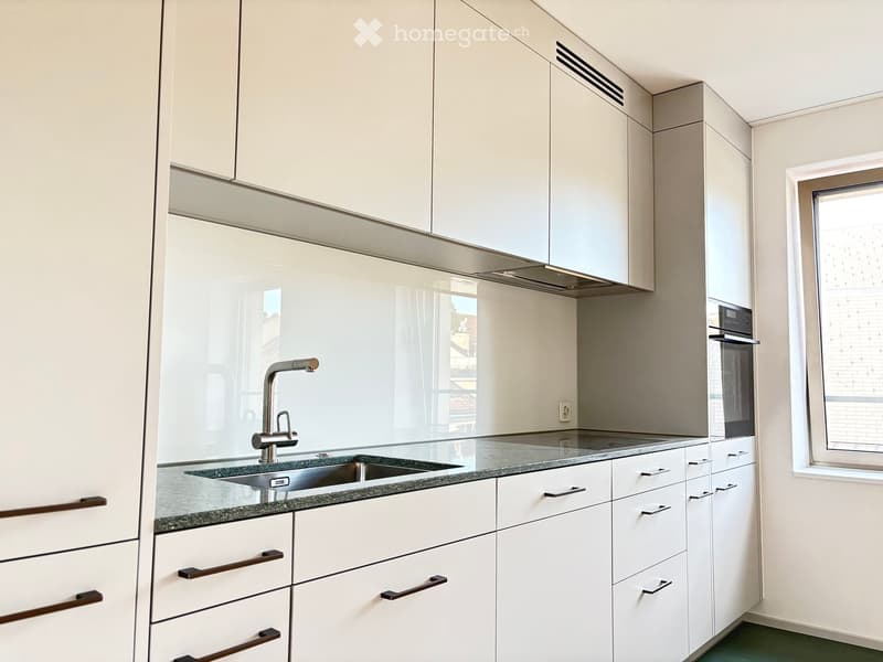 Modern kitchen with white cabinets, granite countertop, stainless steel sink, and built-in oven.