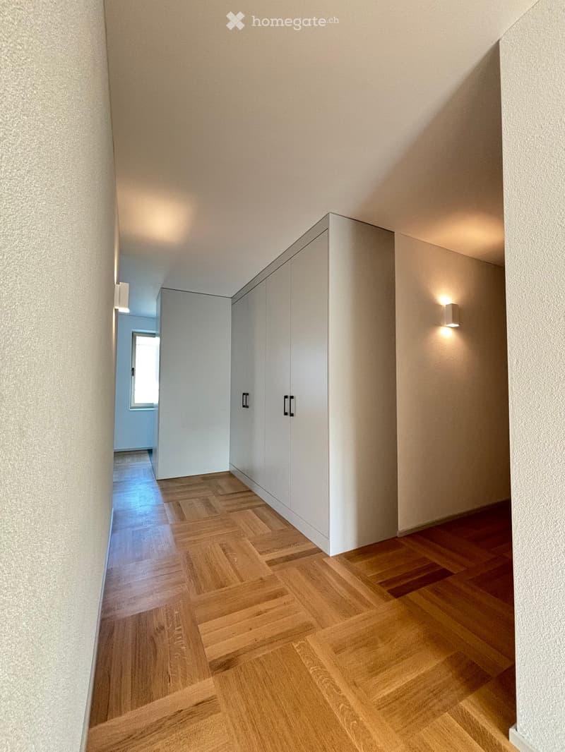 Modern hallway with light wooden herringbone flooring, white built-in closet with black handles, and recessed lighting.