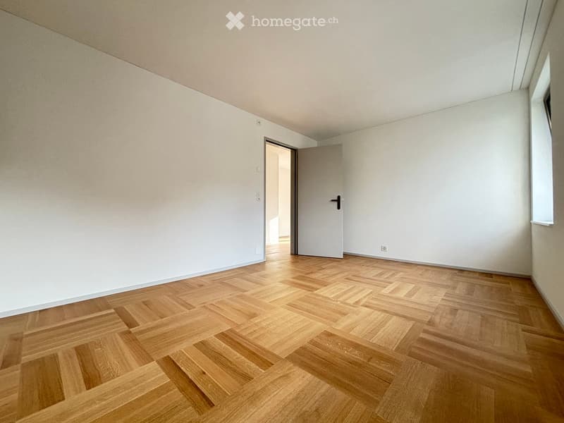 Empty room with light-colored walls and a wooden parquet floor, featuring a door and visible electrical outlets.