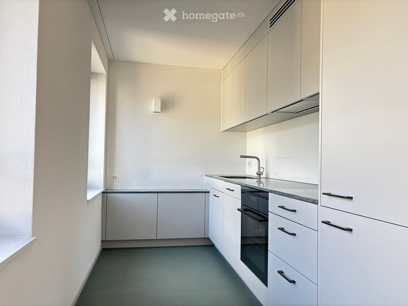 Modern kitchen with white cabinets, dark countertops, and stainless steel appliances including a sink and oven.