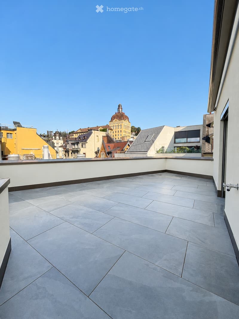 Roof terrace with grey tiled flooring, white low wall, and cityscape view in the background.
