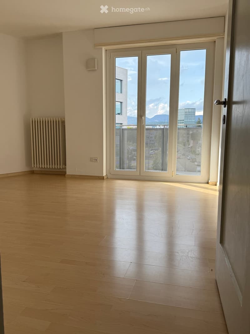 Empty room with light wooden flooring, white walls, and large sliding glass doors leading to a balcony with a scenic mountain view.