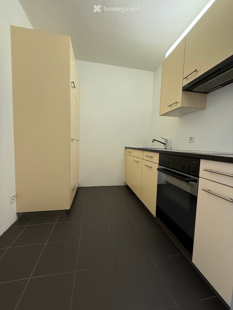 Modern kitchen with light-colored cabinets, black tiled floor, sink, faucet, and built-in oven.