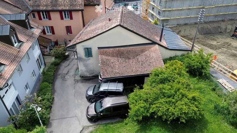 Aerial view of a residential area showing a multi-story building with a garage, several parked cars, and surrounding greenery.