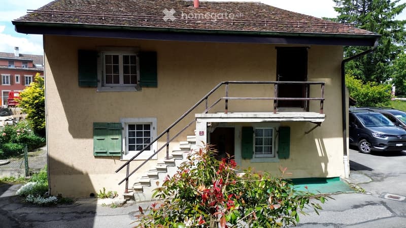 Two-story house with beige exterior, green shutters, and a small balcony accessible via stairs.
