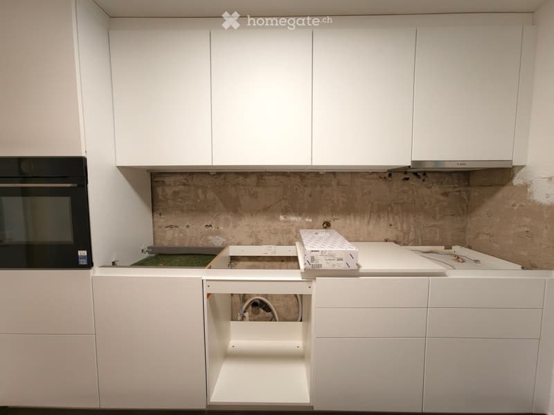 Modern kitchen with white cabinets, an oven, and exposed wiring in an unfinished state.