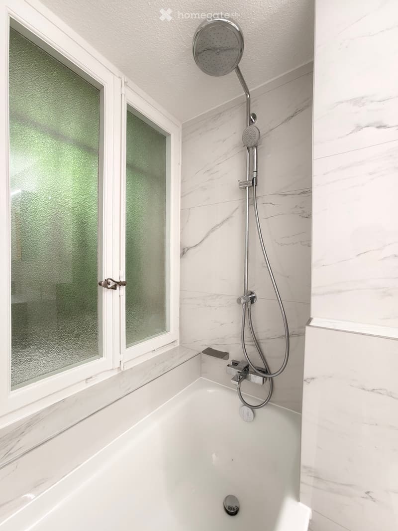 Modern bathroom with a white marble bathtub, a handheld showerhead, and a sleek chrome faucet.