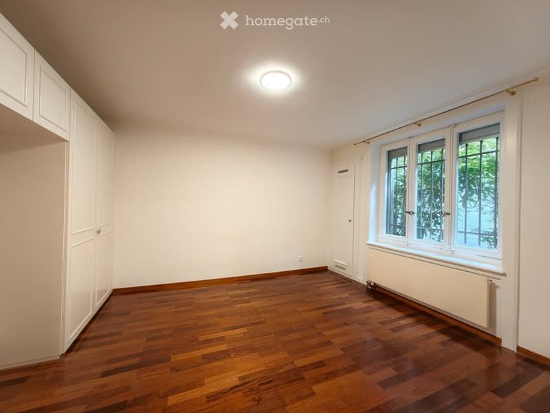 Empty room with wooden flooring, white walls, large windows, and built-in cabinets.