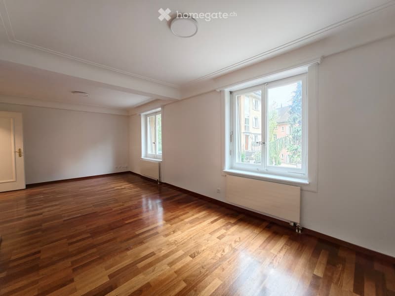 Empty room with wooden flooring, white walls, large windows, and radiators. No furniture or equipment present.