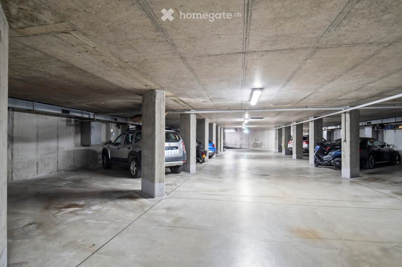 Underground parking area with several parked cars and motorcycles, concrete pillars, and lighting.