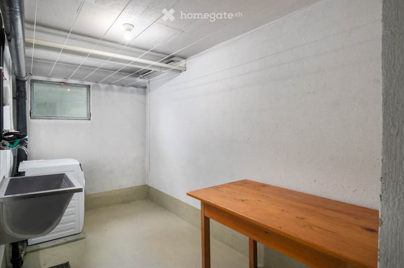A small utility room with a wooden table, a washing machine, and a sink.